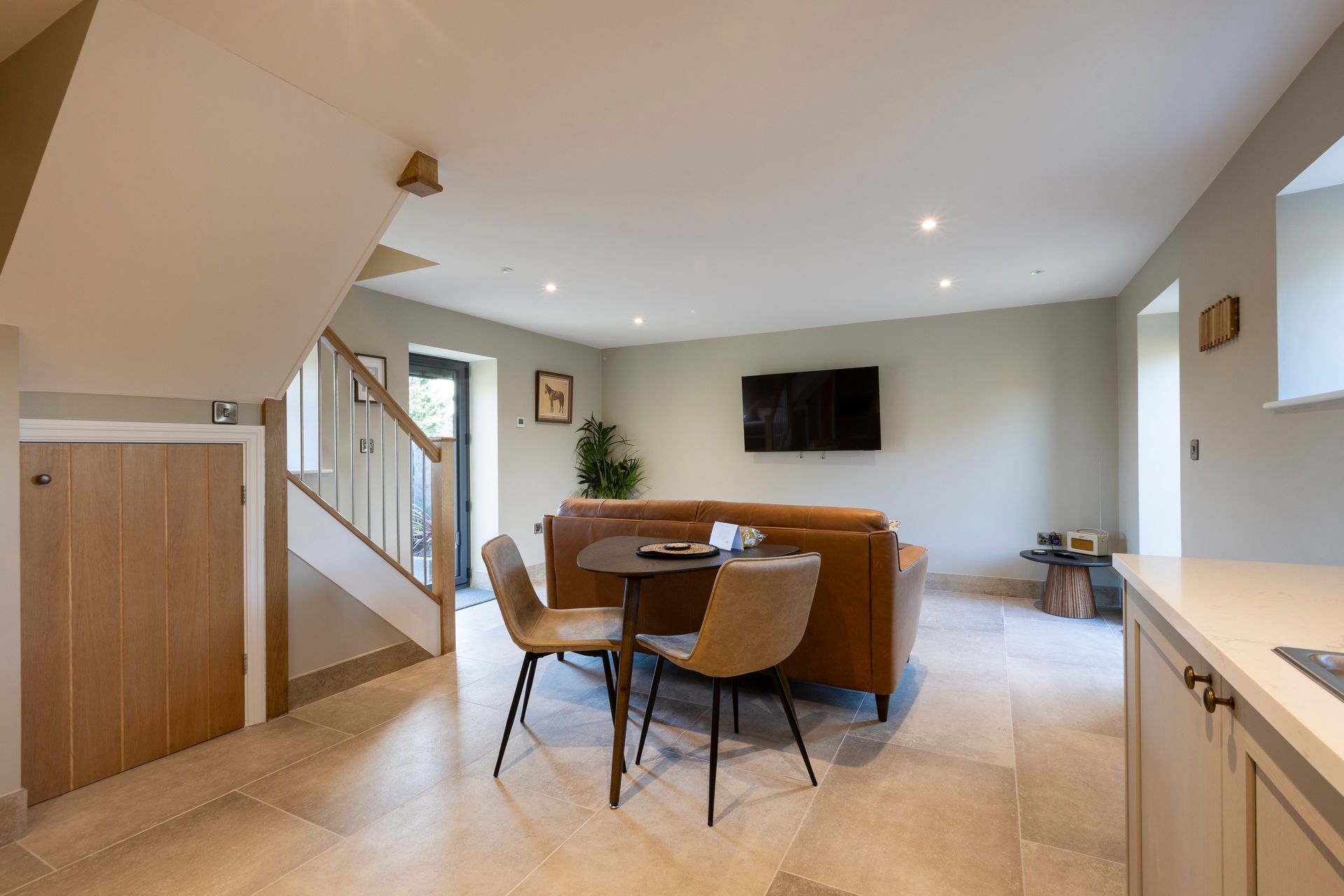 Spacious modern living room with sofa, dining table, wall-mounted TV, and staircase