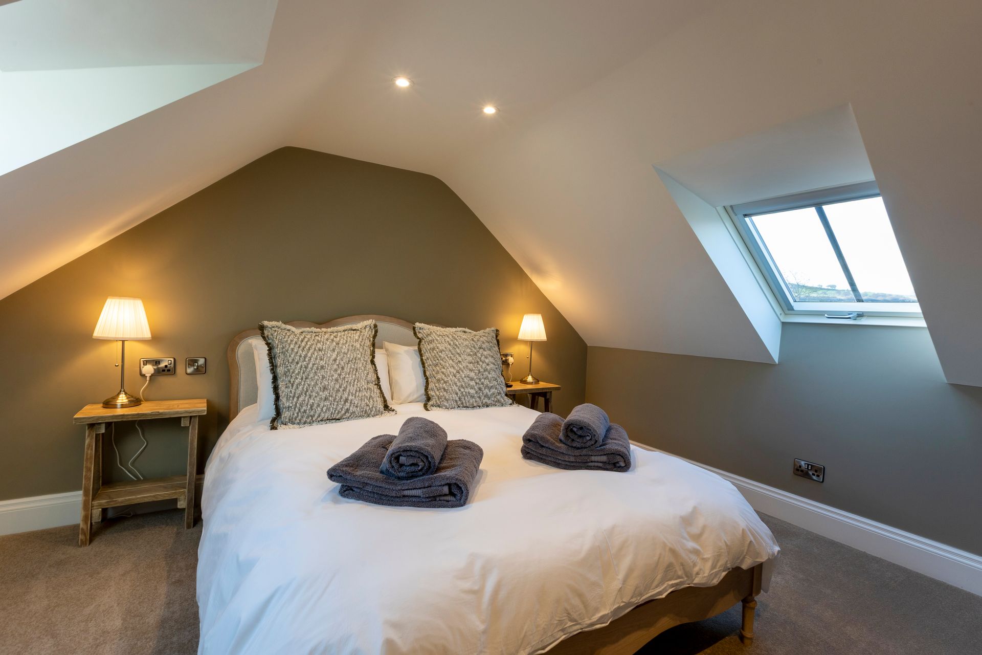 Cozy attic bedroom with a king bed, bedside lamps, and a skylight window