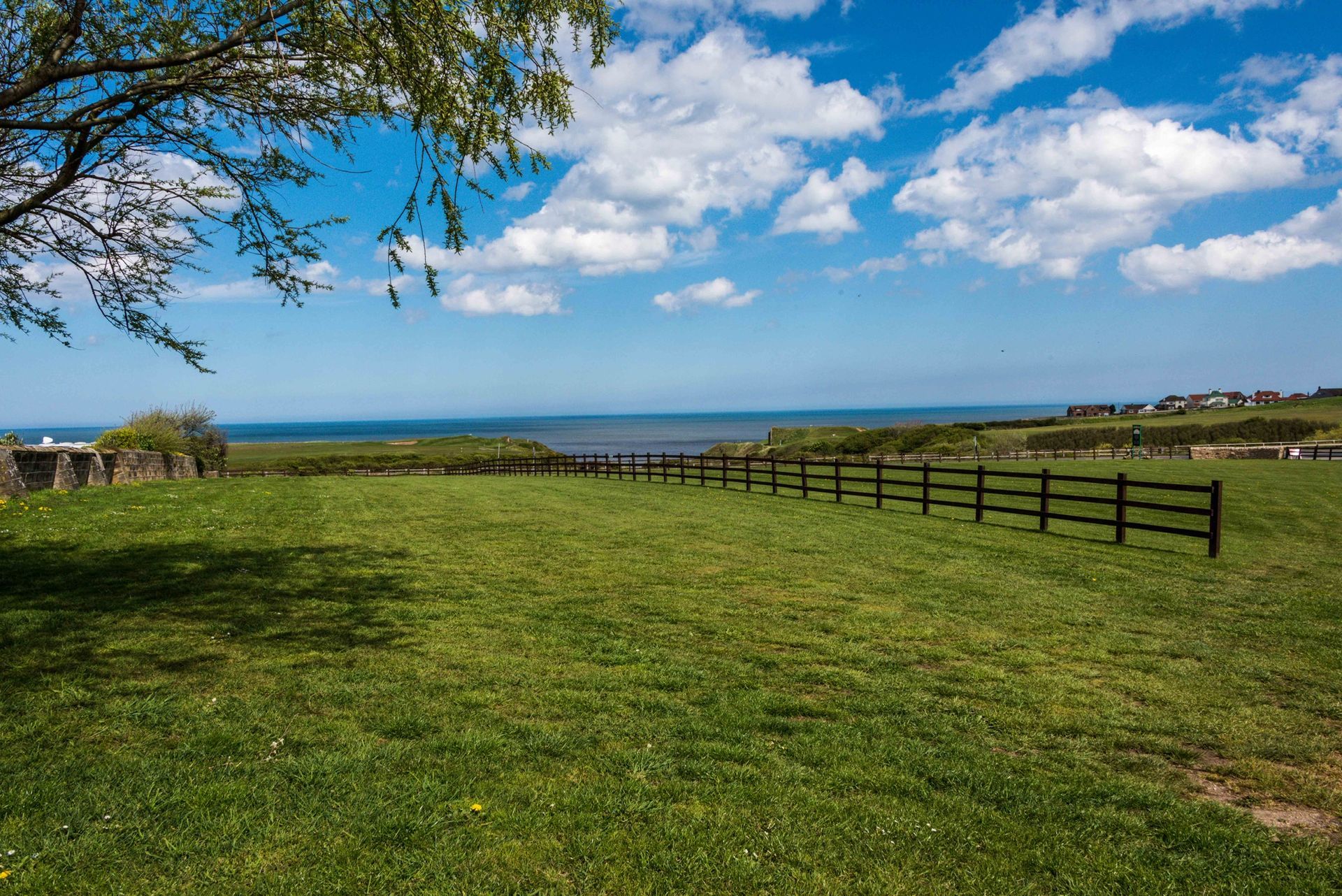 A fence surrounds a grassy field with a view of the ocean.