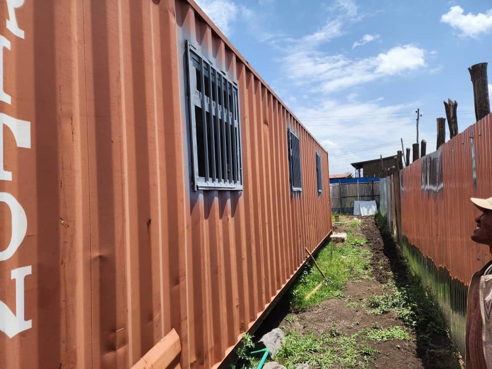 A man is standing next to a shipping container with a window.