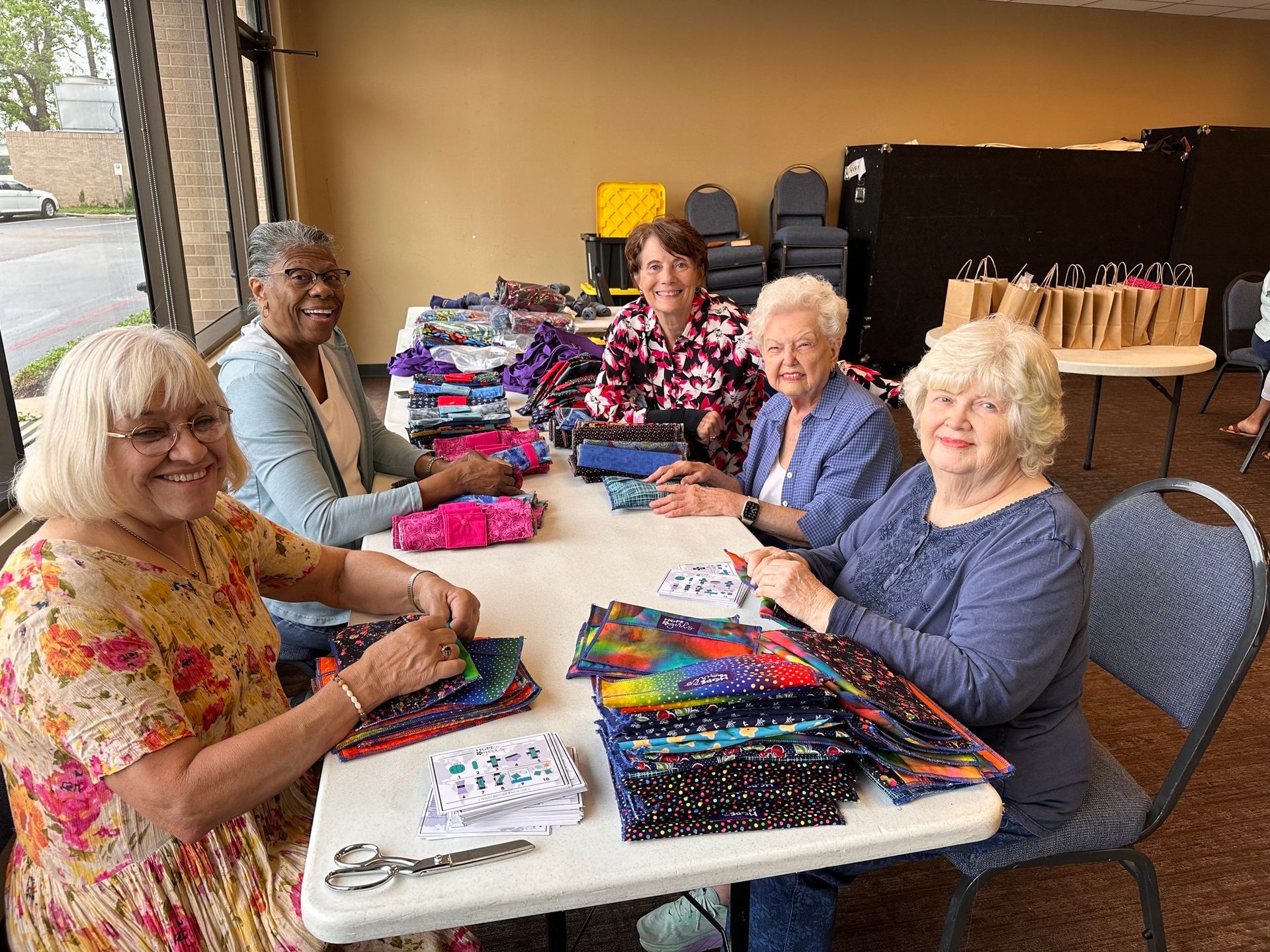 A group of women are sitting at a table making quilts.