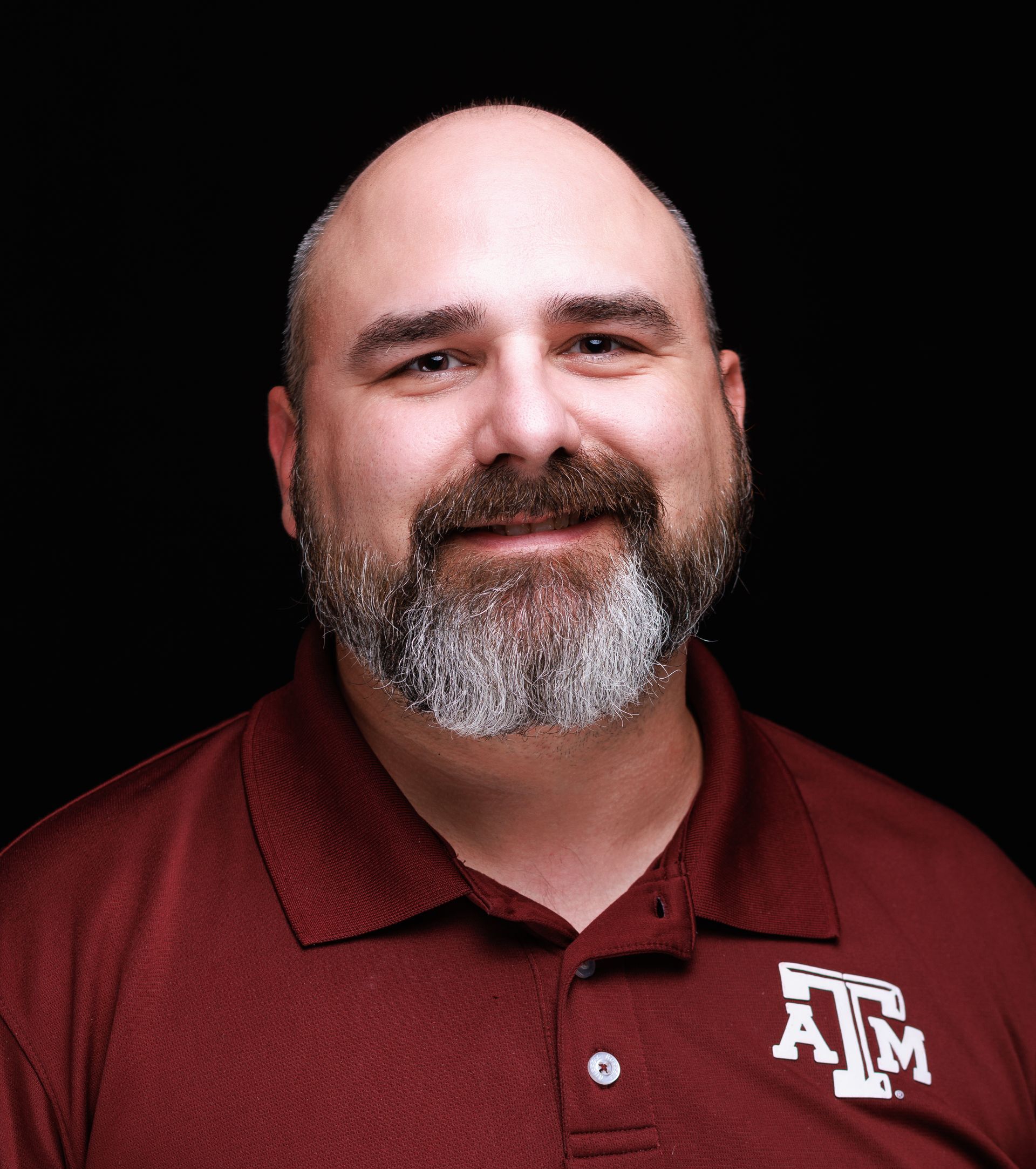 A man with a beard is wearing a maroon atm polo shirt.