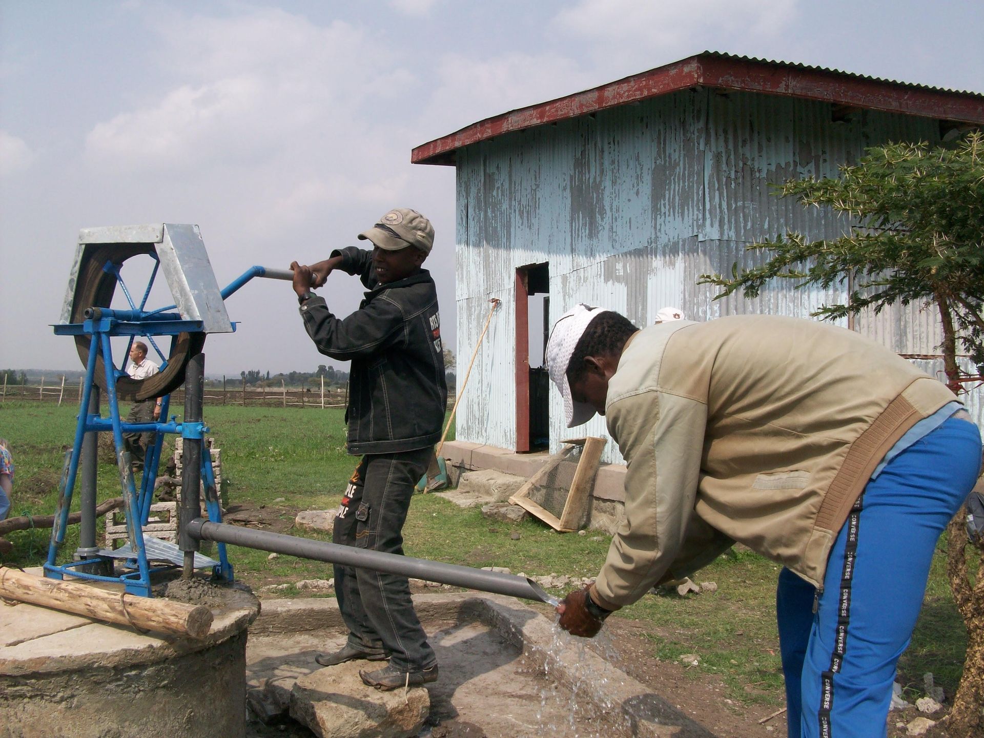 Two men pumping water from a well in front of a building