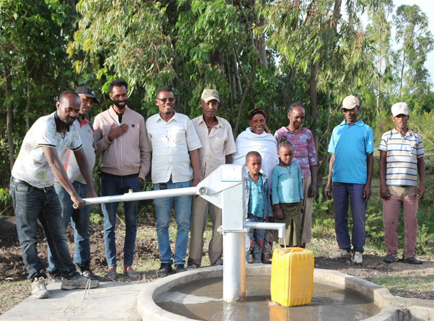 A group of people are standing around a water pump.