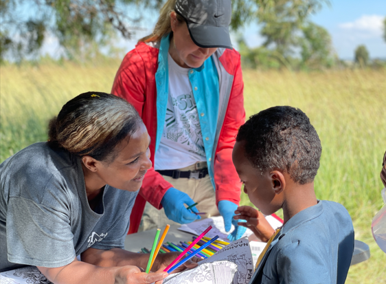 A group of people are sitting in a field playing with straws.