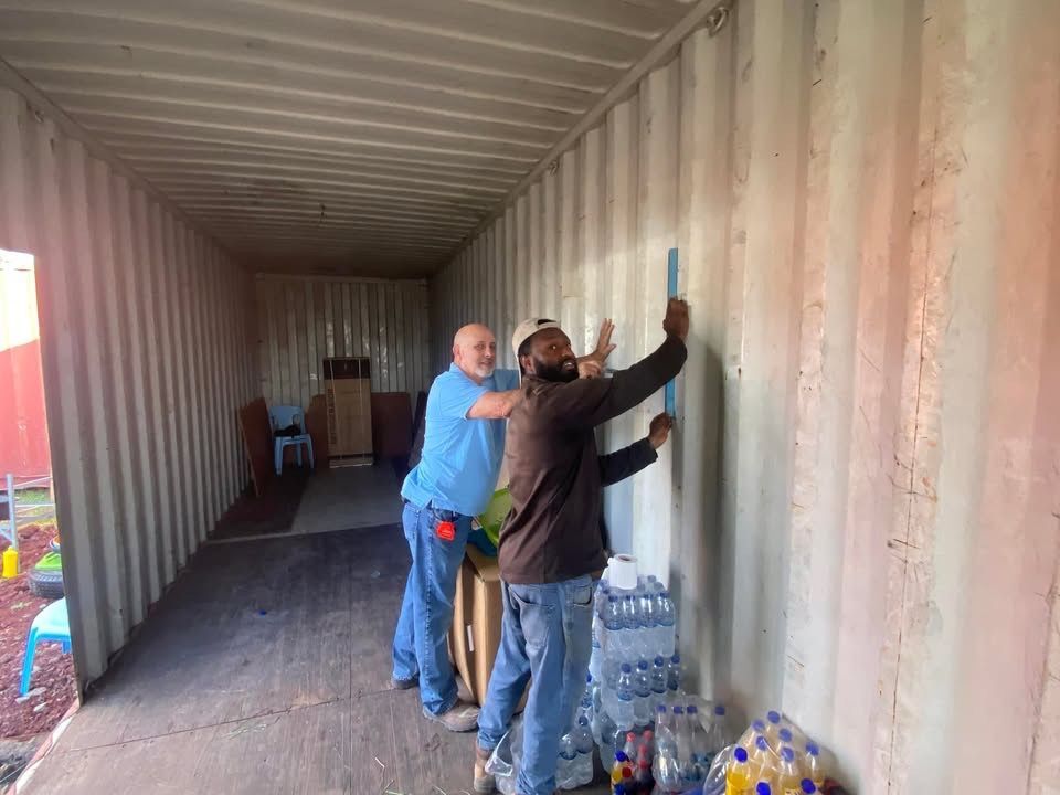 Two men are measuring a wall in a shipping container.