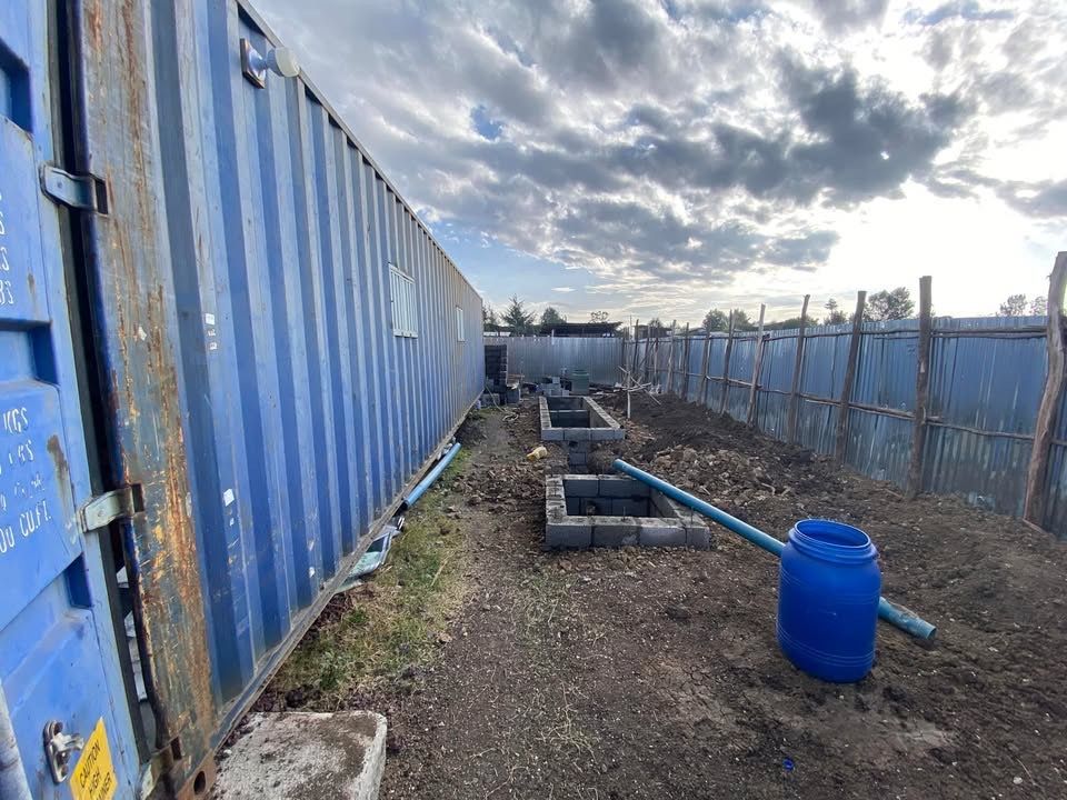 A blue container is sitting in the dirt next to a blue barrel.