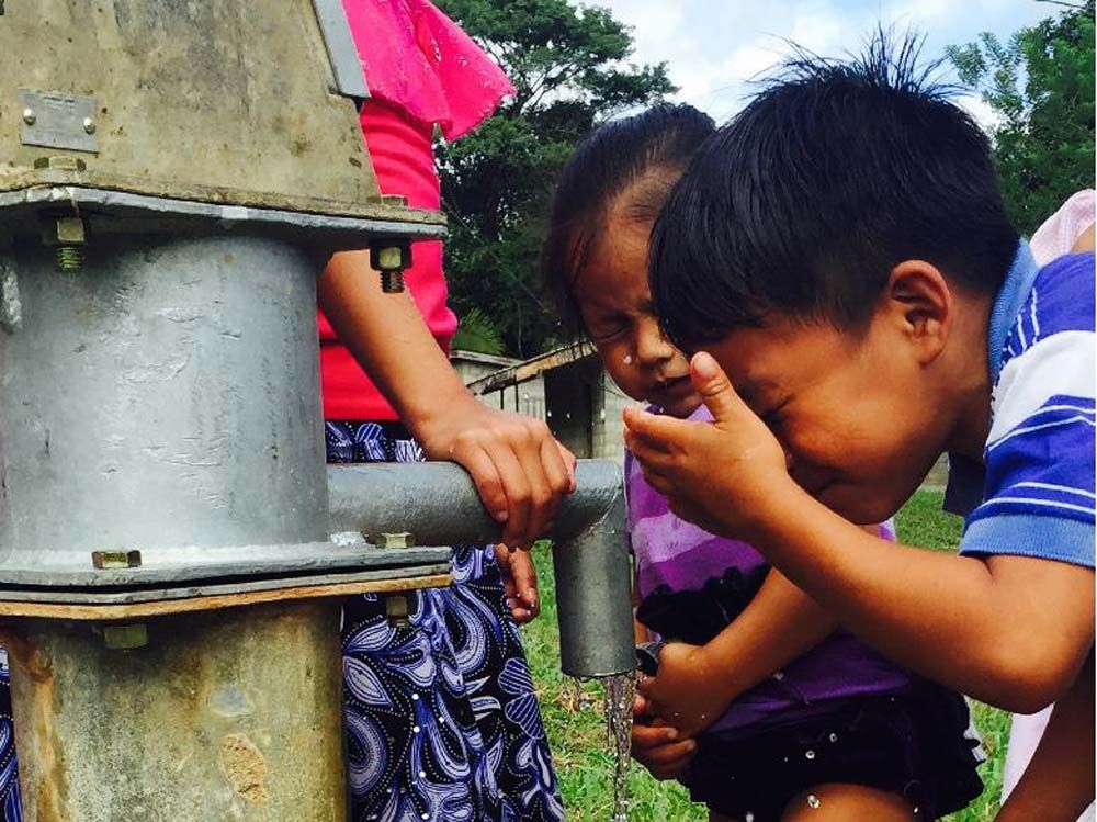 A boy and a girl are drinking water from a well