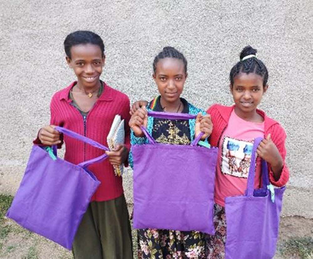 Three young girls are holding purple bags in front of a wall