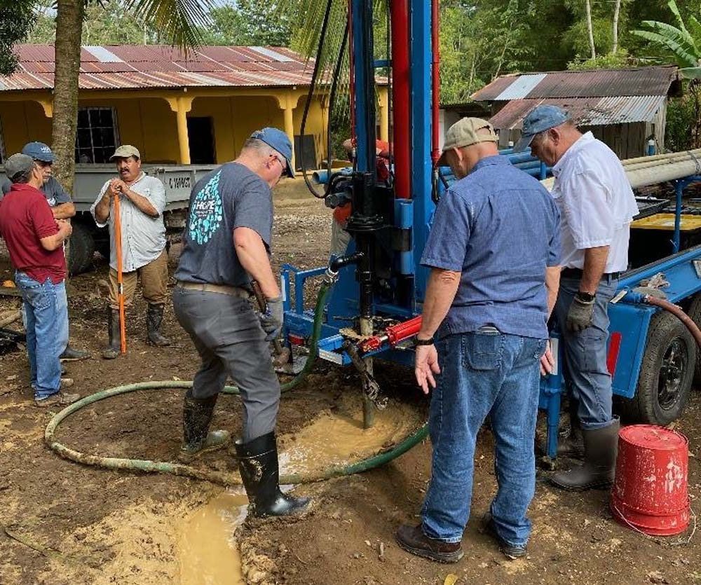 A group of men are standing around a machine in the dirt.