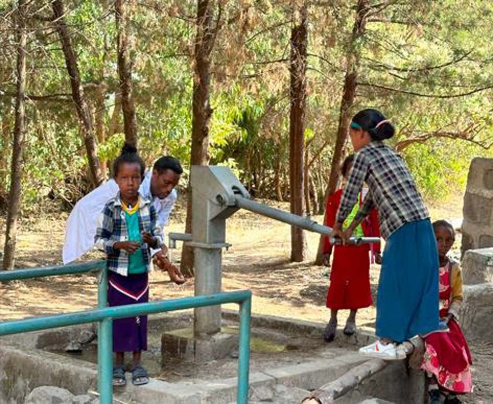 A group of people are standing around a water pump.