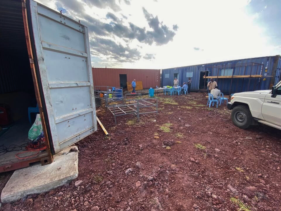 A truck is parked in front of a building in a dirt field.