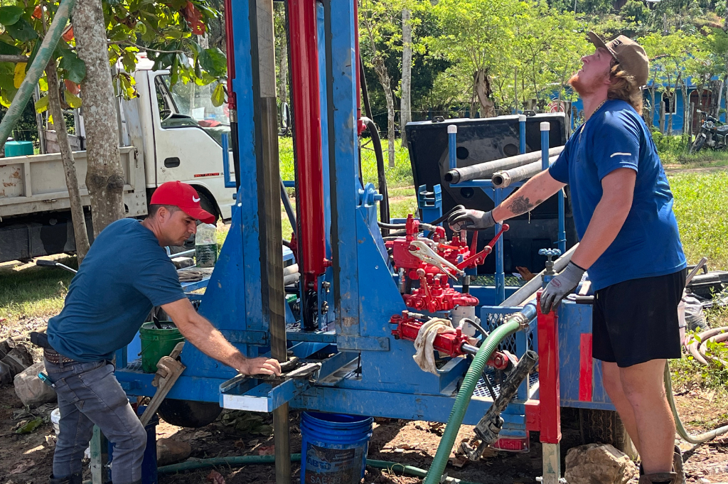 Two men are working on a machine in a field.