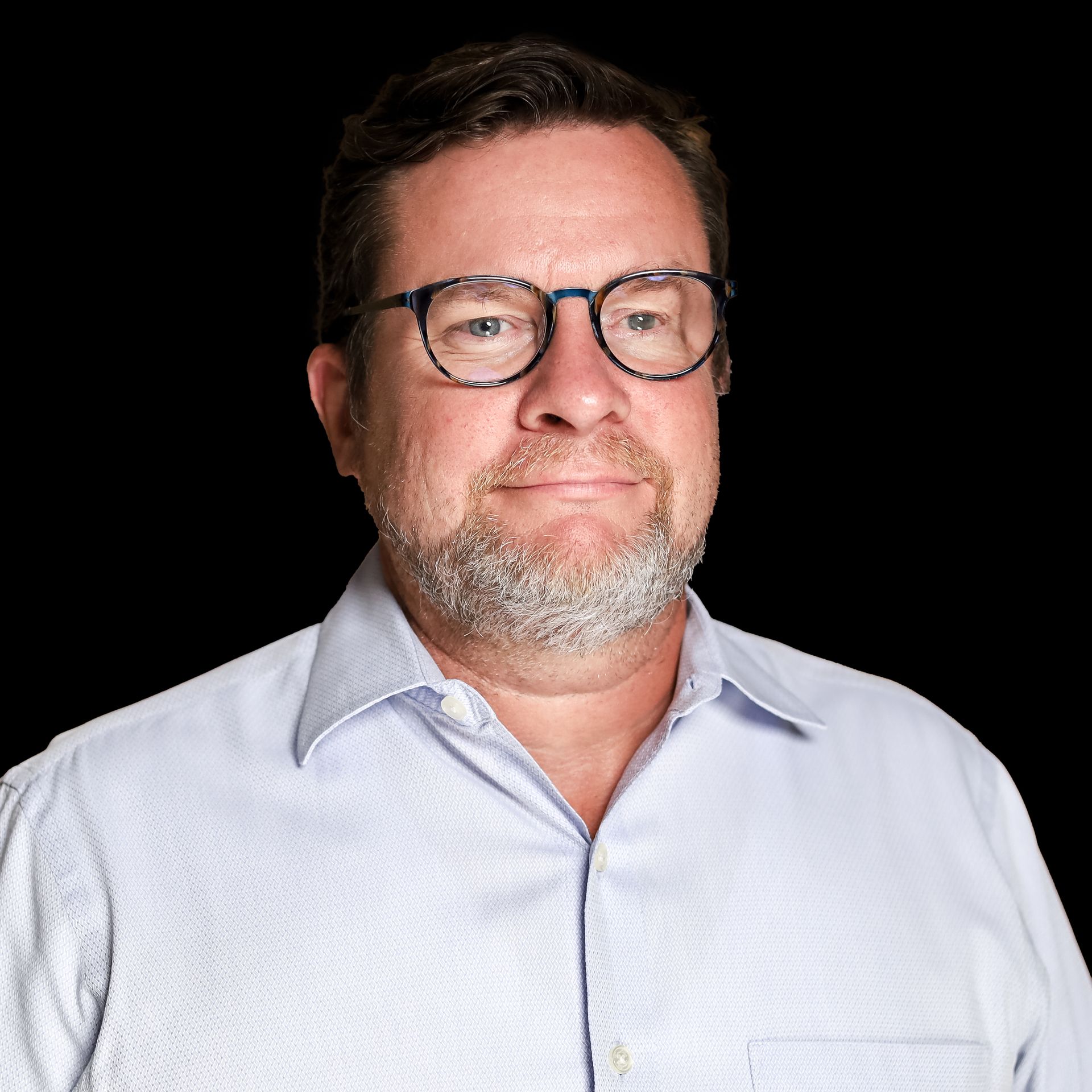 A man with a beard and glasses is wearing a blue shirt.