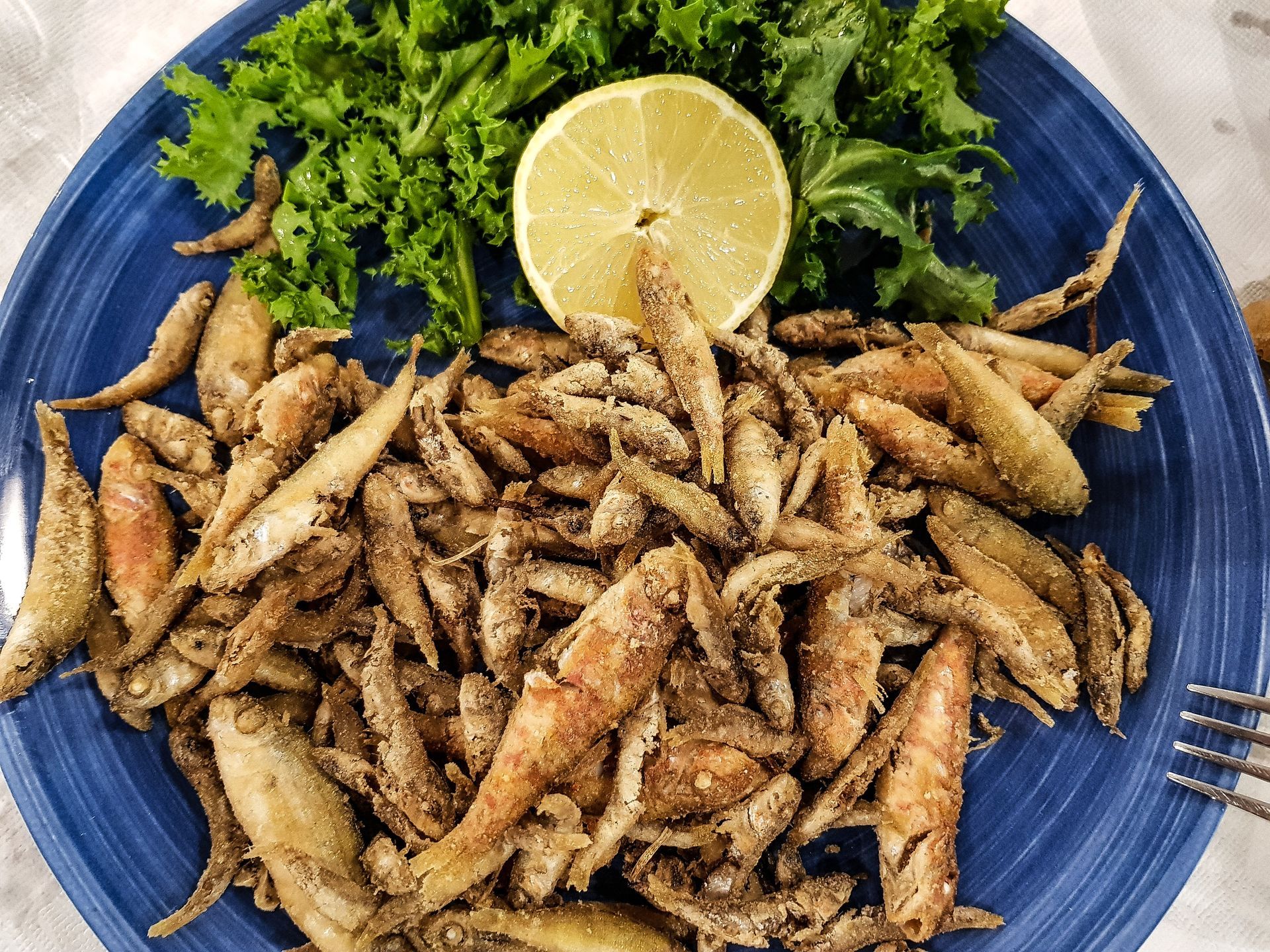 Un piatto blu con sopra pesce fritto, lattuga e una fetta di limone.