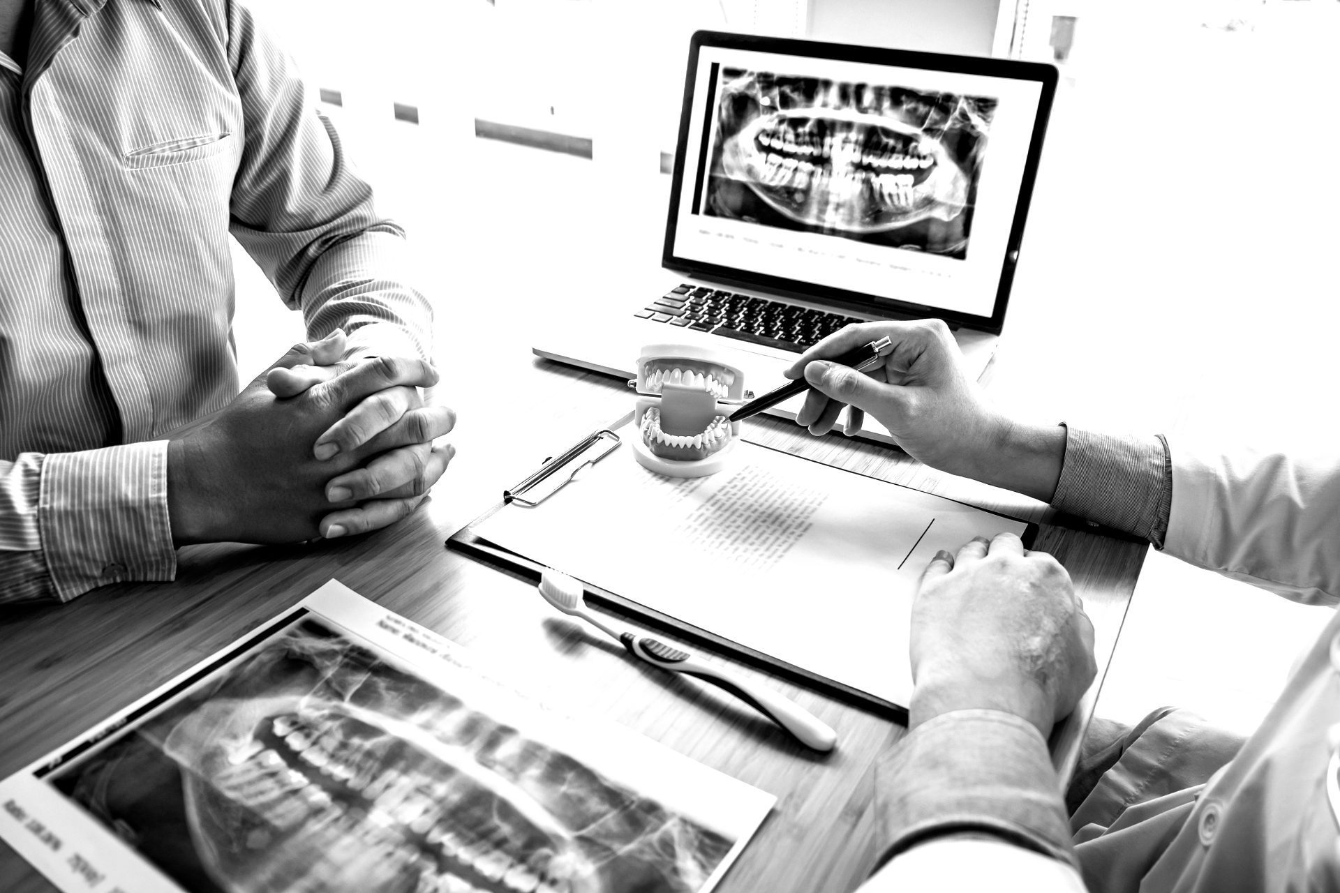 Doctors reviewing dental X-rays and treatment notes at a desk with a patient model and laptop screen