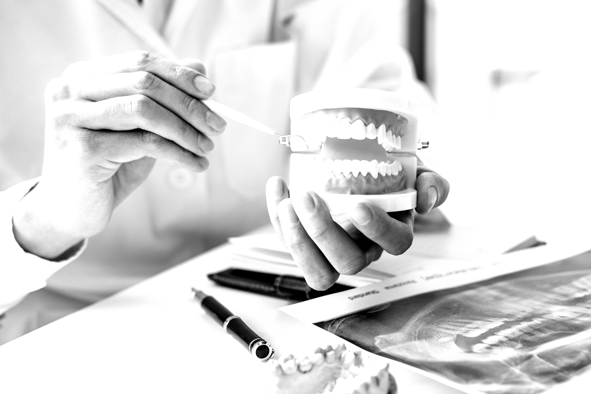 Dentist demonstrating dental model with tool beside X-ray and pen on desk