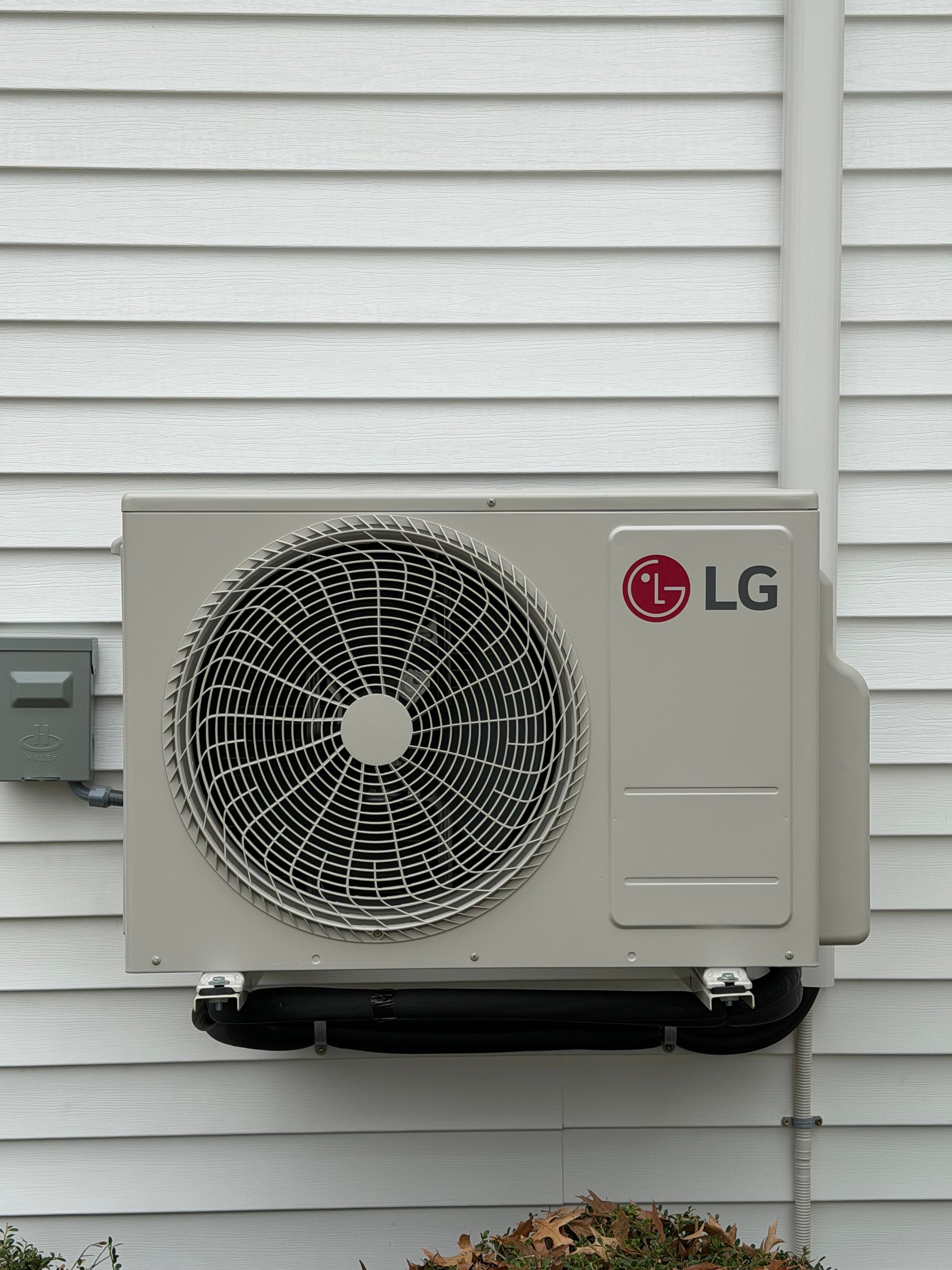 LG outdoor air conditioner unit mounted on a white siding wall with visible fan grille.