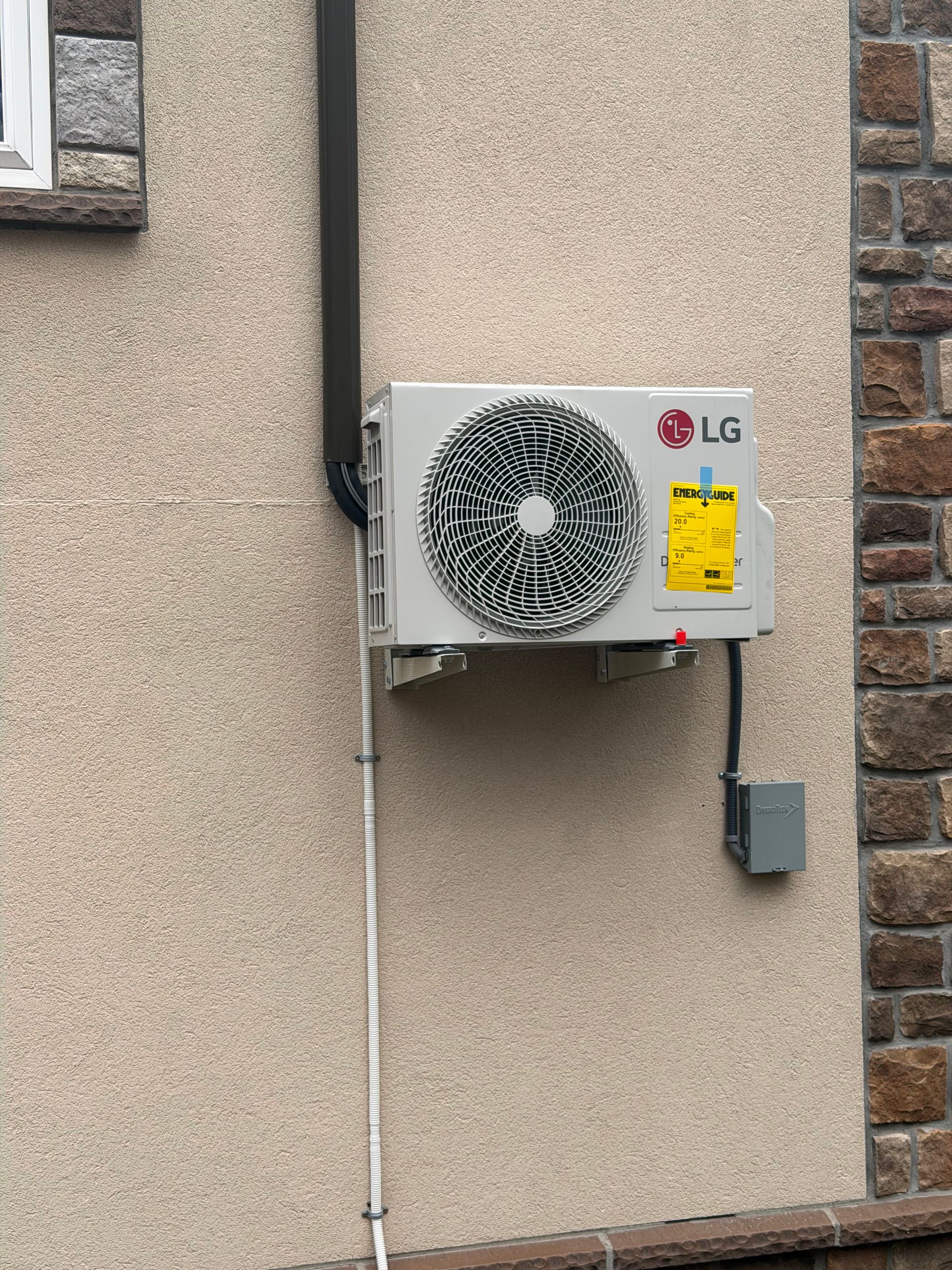 LG outdoor air conditioner unit mounted on a stucco wall with visible piping and electrical box