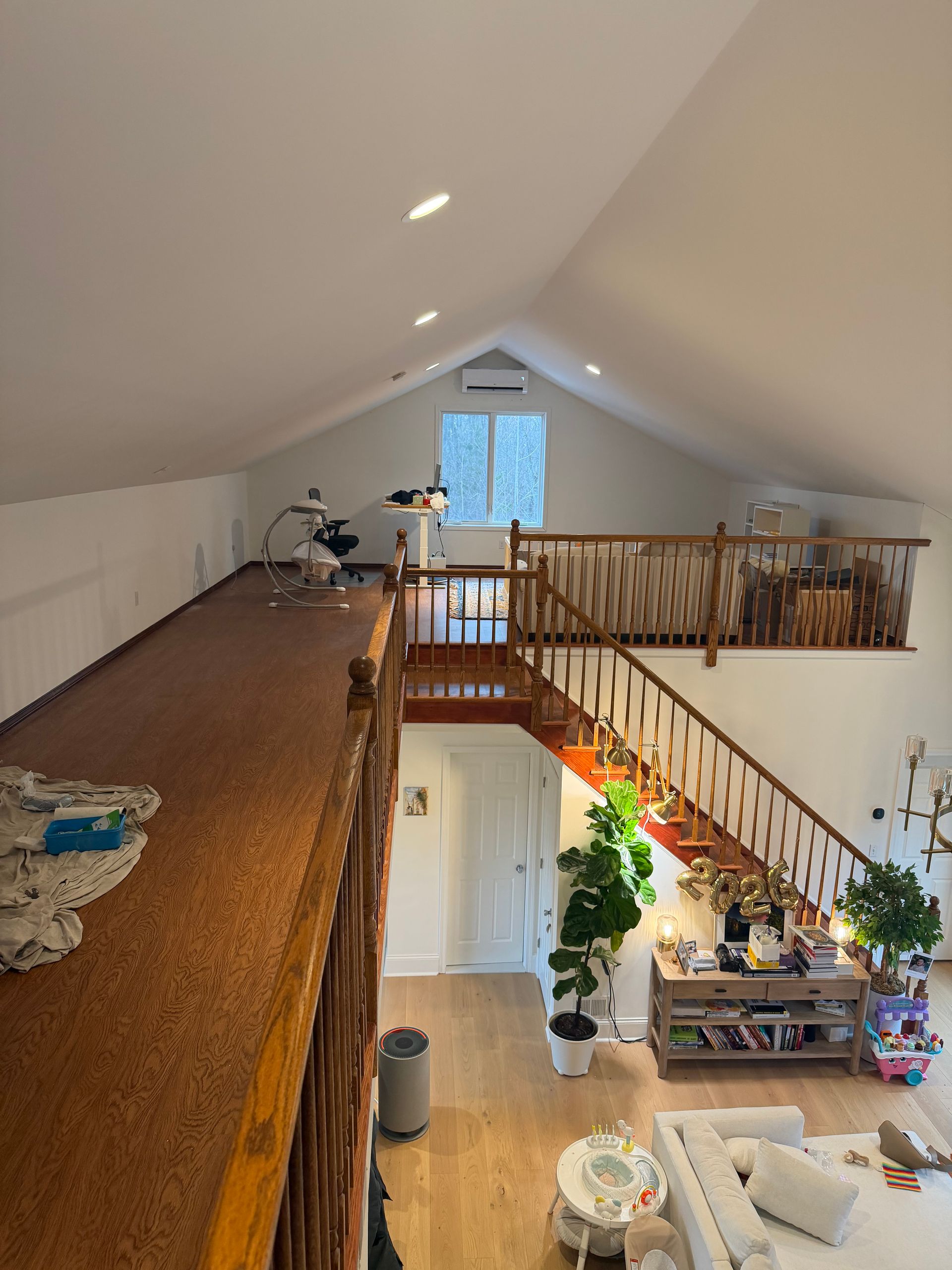 Loft interior with sloped white ceiling, wood railing, staircase, and living area below