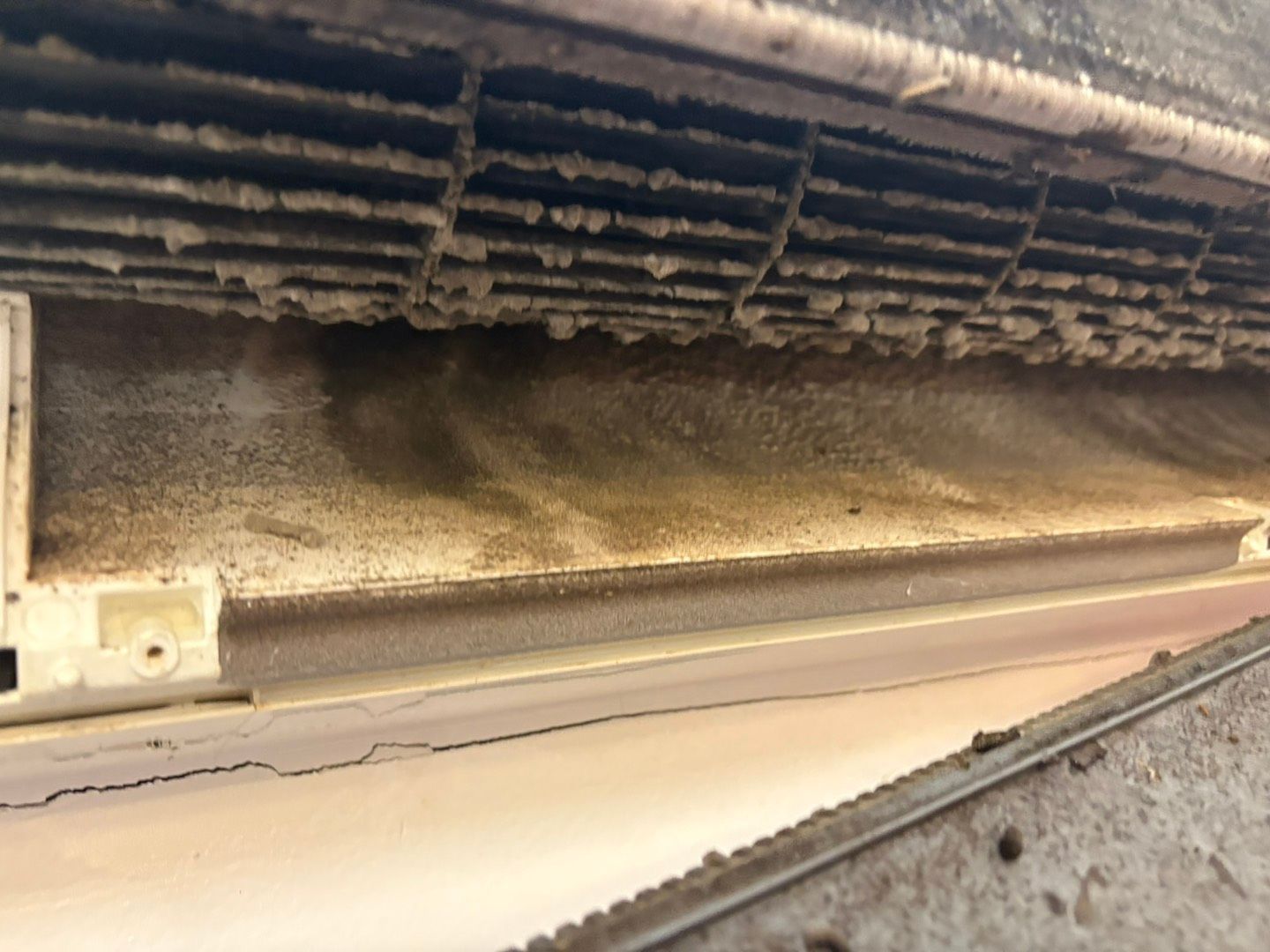 Close-up of dusty industrial machinery with grime and worn metal parts under a conveyor belt