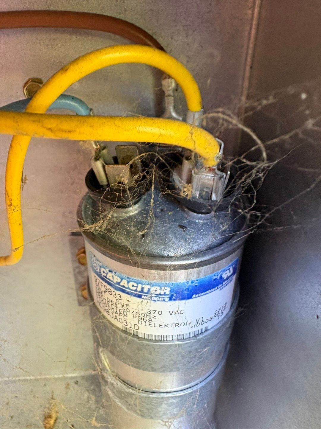 Dusty metal canister with yellow hoses and tangled wires in a cramped utility space