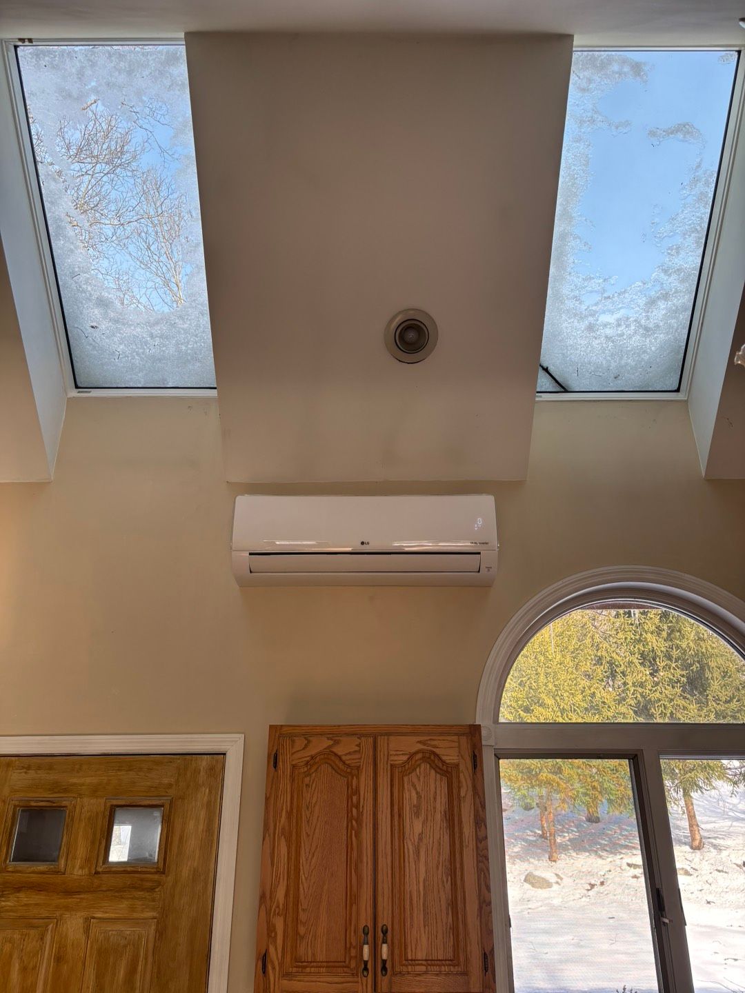 Interior with skylights, a wall-mounted AC unit, wooden doors, and an arched window overlooking trees.