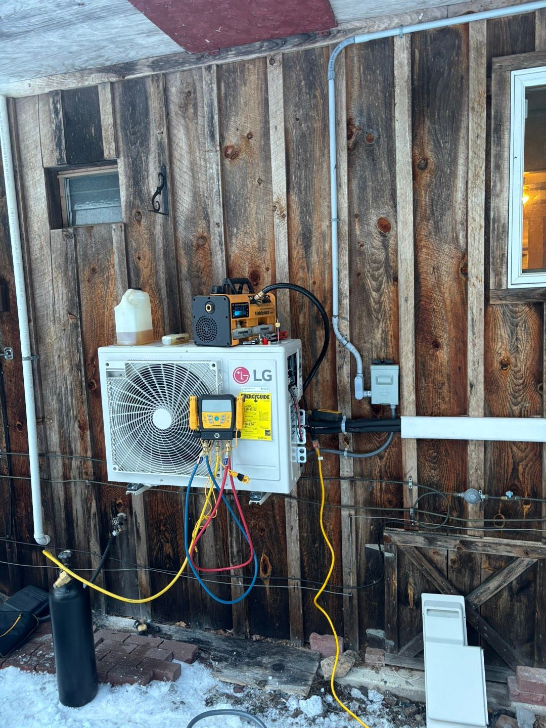 LG wall-mounted electrical box with exposed wiring on an outdoor wooden wall in snow