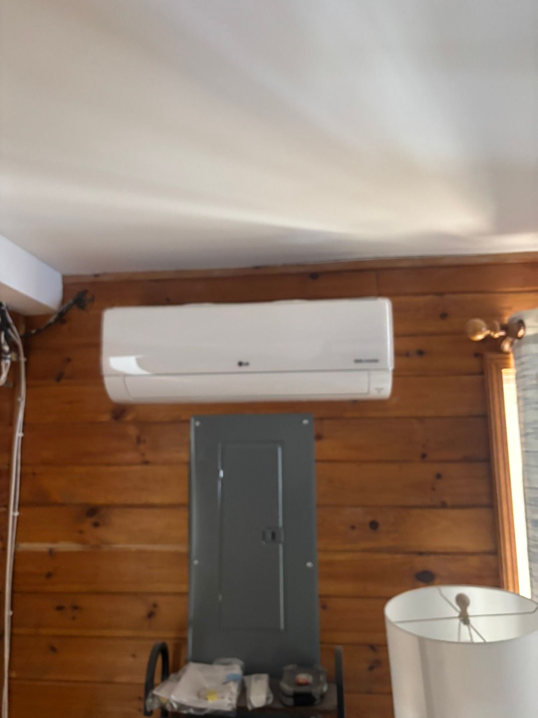 Wall-mounted white air conditioner above a gray cabinet in a wood-paneled room.