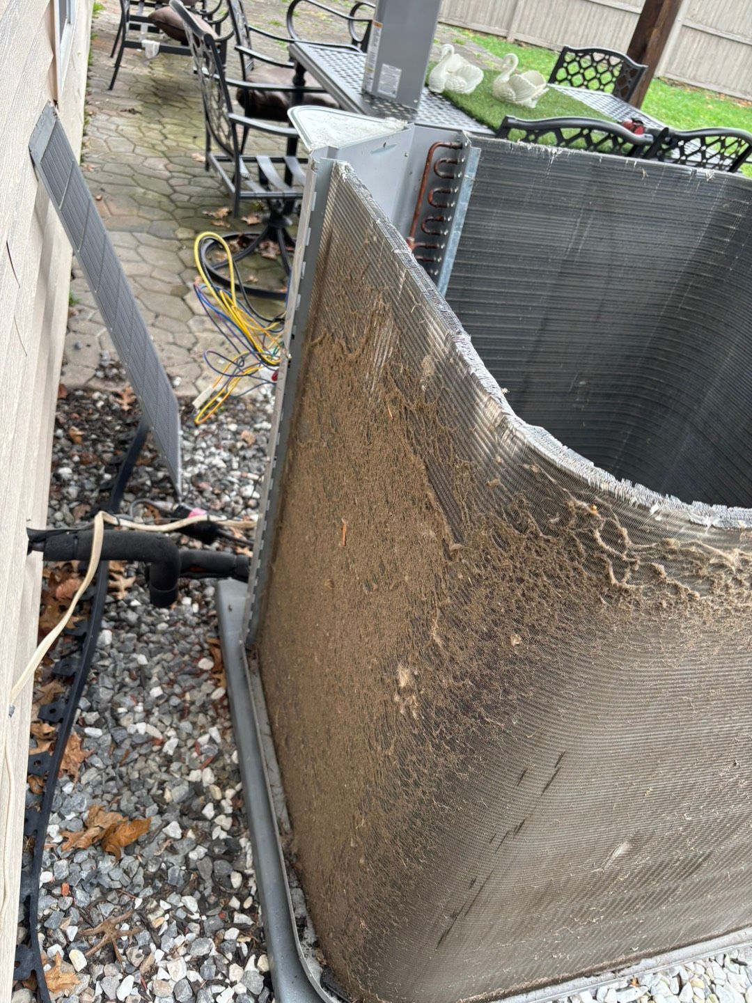 Outdoor HVAC unit beside a house, with a bent metal panel and debris on the ground.