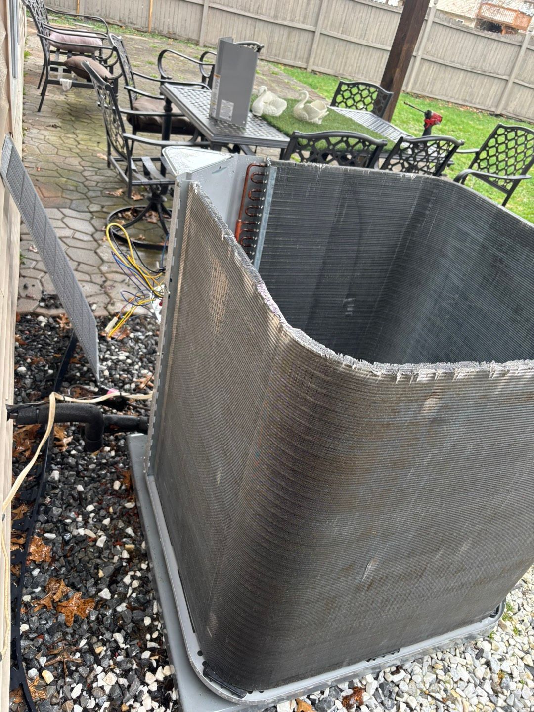 Outdoor patio with a damaged square planter beside a grill, chairs, and a wooden fence.