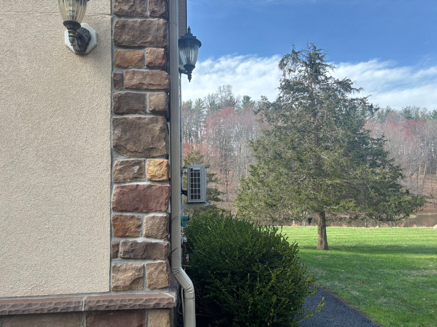 Corner of a house with stone and stucco, wall lanterns, and a view of trees and lawn outside