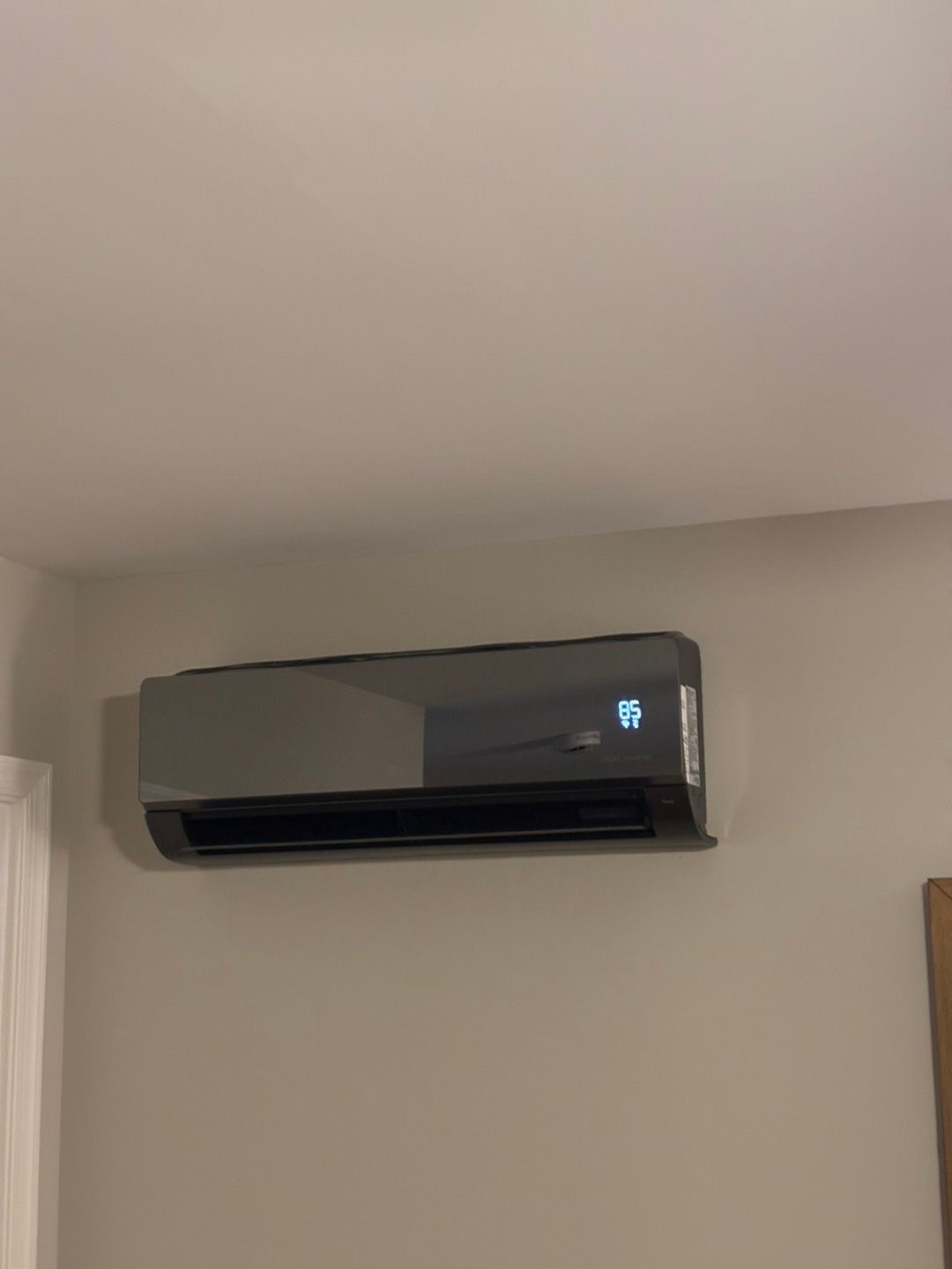 Wall-mounted gray air conditioner on a beige wall in a room corner.