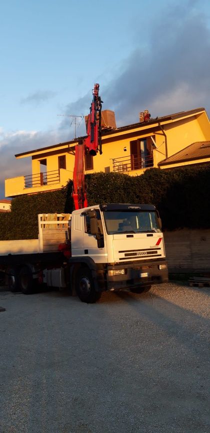 Un camion bianco con gru è parcheggiato accanto a un edificio giallo al tramonto.