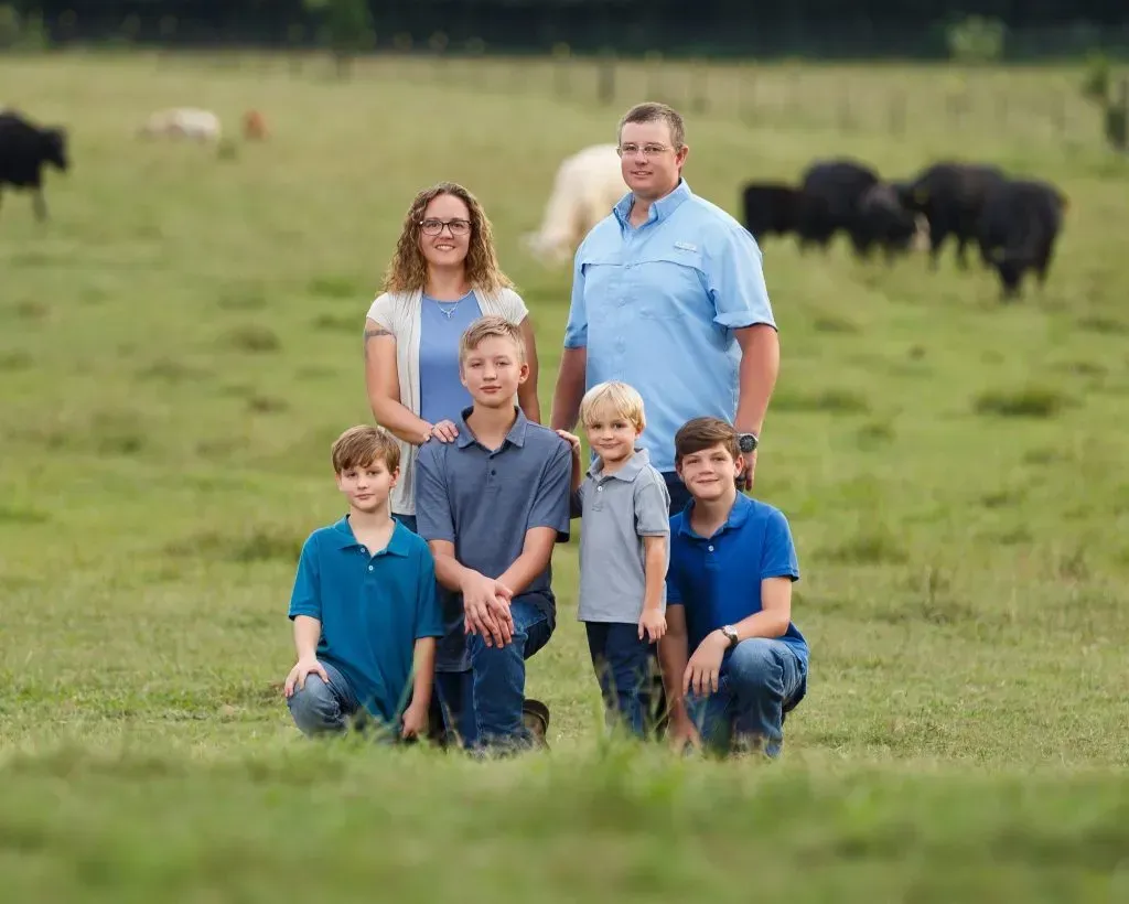 Family of six, posing in a green field with cows in the background.