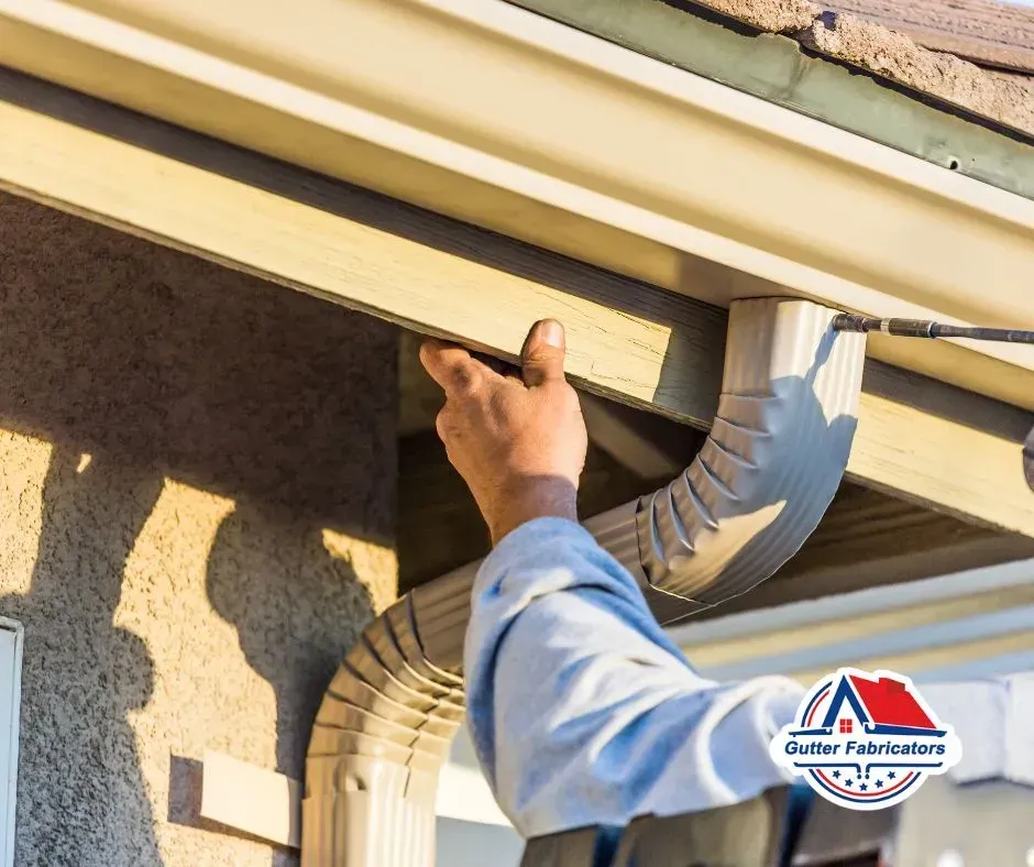 Person installing a light-colored gutter system on a house.