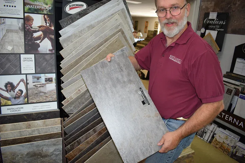A man in a red shirt is holding a tile in his hands.