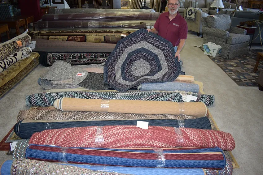 A man is holding a rug in front of a pile of rugs