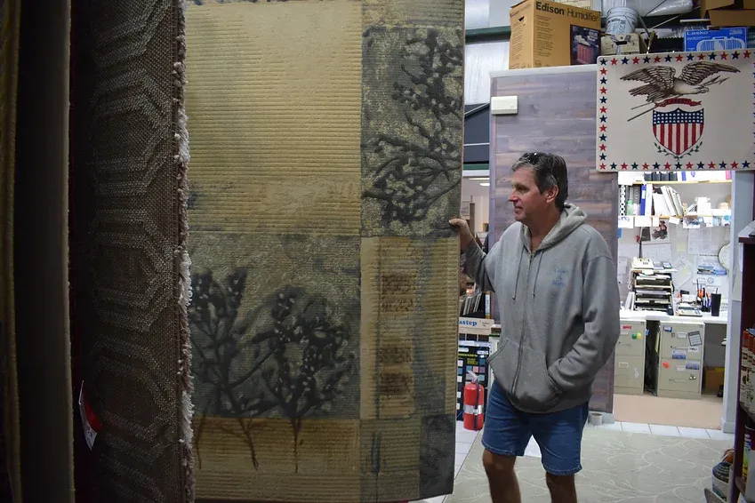 A man in a gray hoodie is standing in a room holding a piece of paper.