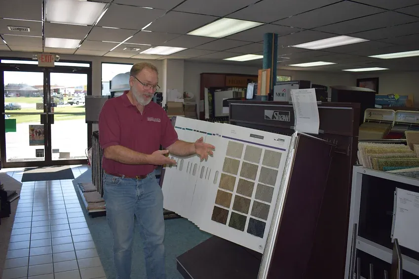 A man in a red shirt is standing in front of a display of tiles