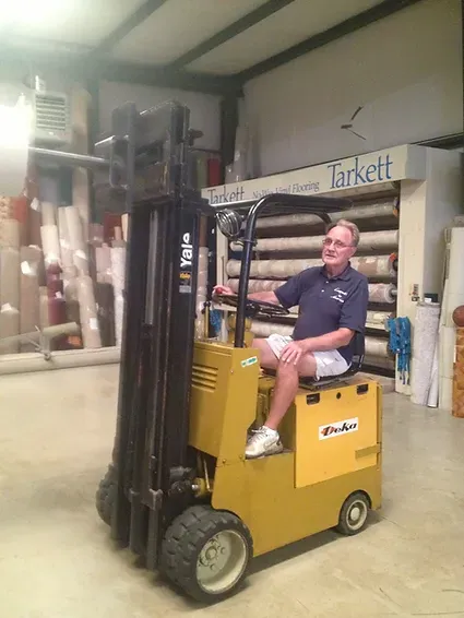 A man is sitting on a yellow forklift in a warehouse.
