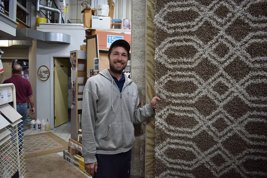 A man is standing next to a rug in a store.