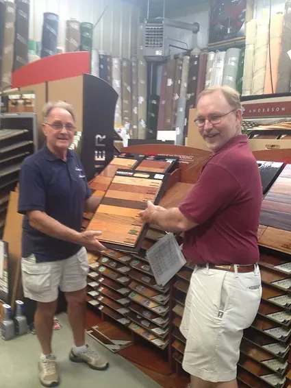 Two men are standing in a store holding samples of wood flooring