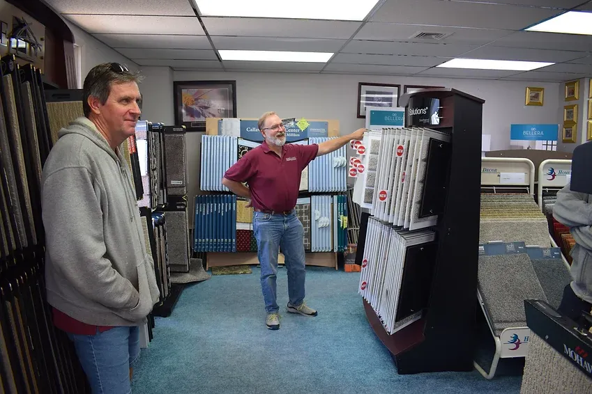 Two men are standing in a carpet store talking to each other