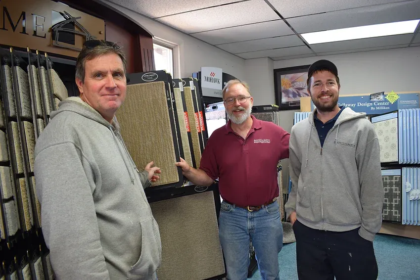 Three men are posing for a picture in a carpet store.