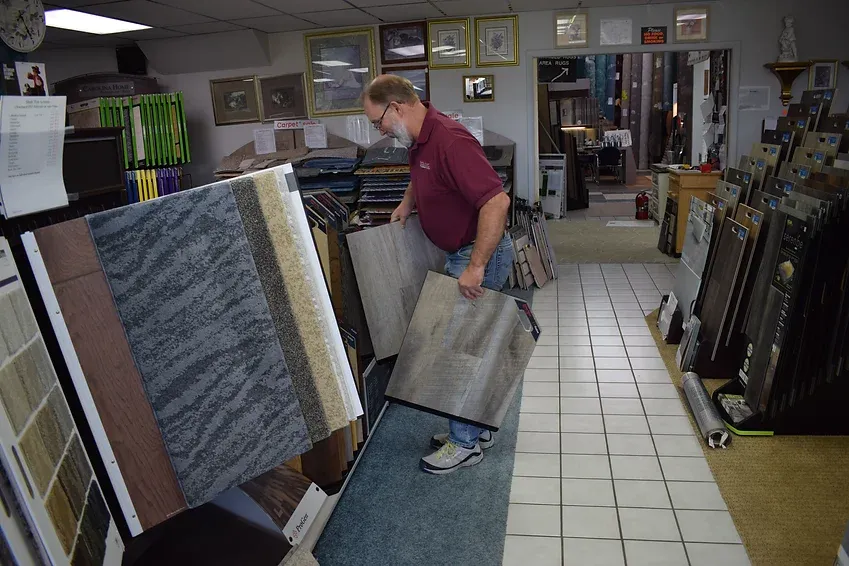 A man is holding a piece of carpet in a store