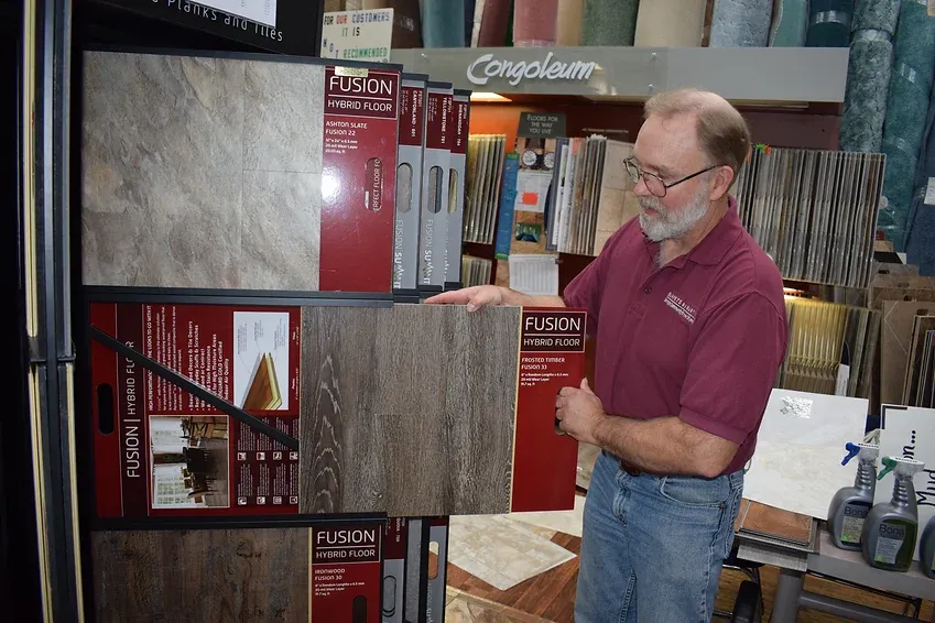 A man in a burgundy shirt is holding a piece of flooring