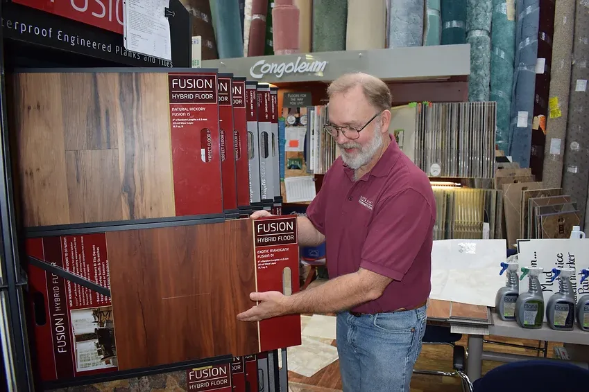 A man in a red shirt is standing in front of a display of flooring