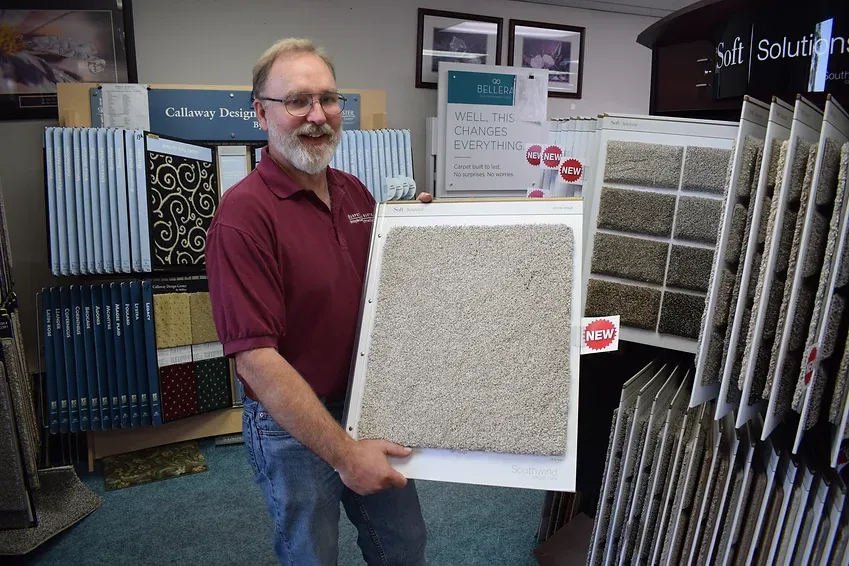 A man in a red shirt is holding a piece of carpet