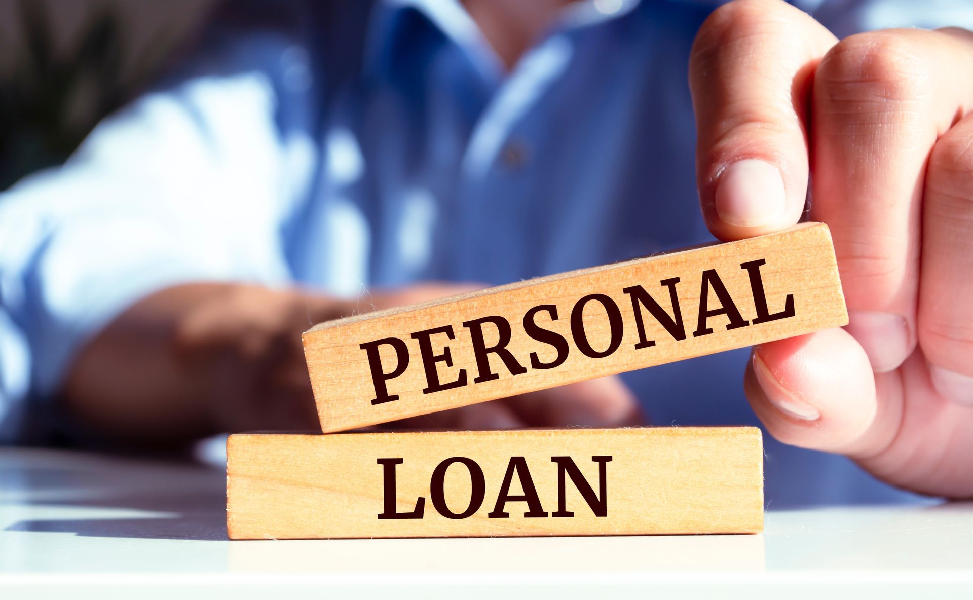 Wooden blocks labeled “PERSONAL LOAN” held in a hand, with blurred office background.